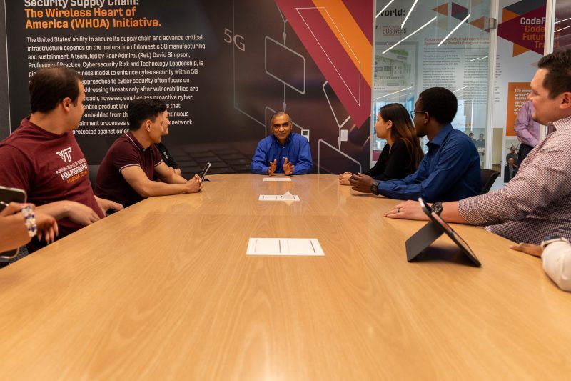 A professor sits and speaks to a group of seated students at a long table